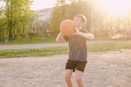 Young boy playing basketball taking aim with the ball at the goal with a look of concentration backlit with flare from the evening sunの写真素材