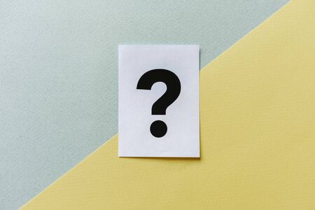 Question mark printed on a page of white paper placed to the center on diagonal yellow grey divided...