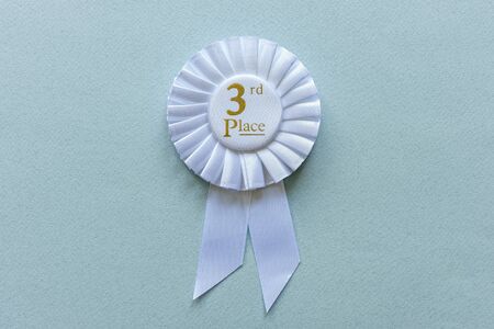 3rd Place white ribbon rosette with gold text for a competition runner up winner on grey with copy...