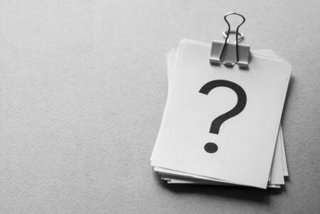 Stack of white cards printed with question marks held together with a metal paper clip over a grey background with copy spaceの写真素材
