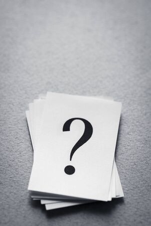 stack of paper cards with a printed question mark on a gray background.