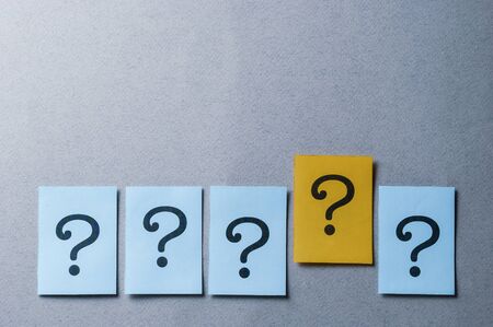 Four question marks on blue and one on yellow arranged in a line on a grey background with copy space in a concept of individuality or leadershipの写真素材