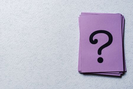 Stack of printed question marks on purple paper arranged to the side on a grey background with copy spaceの写真素材