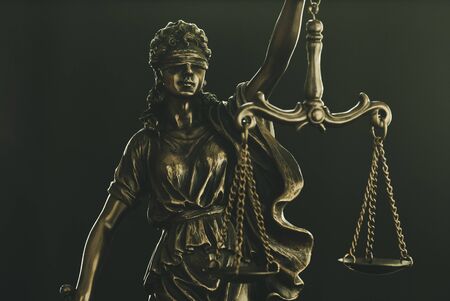 Figure of Justice wearing a blindfold holding up the scales of law over a black background in a close up conceptual viewの写真素材