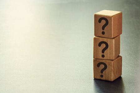 Stack of three wooden cubes with question marks forming a side border over a graduated grey background with copy spaceの写真素材