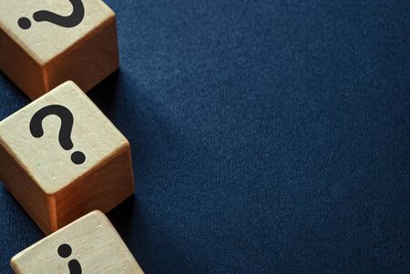 Side border of question marks on wooden cubes over a dark blue textured background with copy space