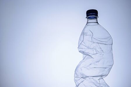 Crumpled clear empty plastic bottle with lid as a side border over blue with copy space conceptual...
