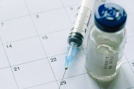 Closed vial with medication and empty syringe on white calendar list background. Vaccination schedule concept with copy spaceの写真素材