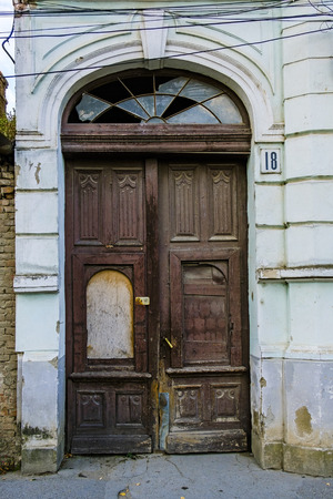 Dilapidated arched double wooden door with broken glass panel at the top as a street entrance to an old building in a close up viewのeditorial素材