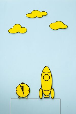 Little yellow rocket on a launch pad with alarm clock alongside and clouds above with copy space, cartoon illustrationの写真素材