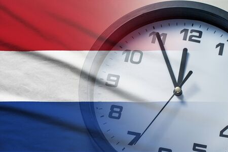 Composite of the Netherlands flag and a clock face counting down to twelve midnight or noon in a conceptual imageの写真素材