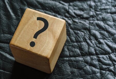 Wooden cube on black leather with question markの写真素材