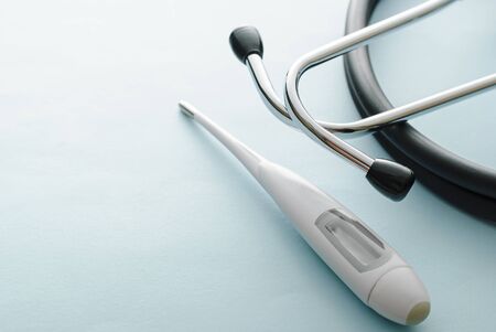 Thermometer and stethoscope on white with copy space in a concept of the diagnosis of the Covid-19 virus due to fever or listening to the heart and lungs during the global coronavirus pandemicの写真素材