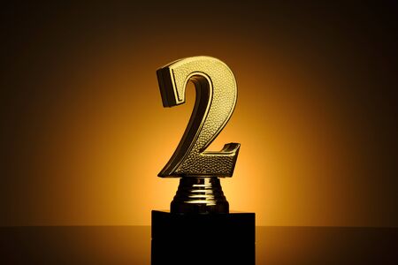 Gold number 2 award trophy for the second place runner up with textured surface on a plinth over a brown background with orange highlightの写真素材