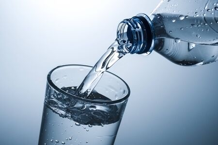 Sparkling water being poured into a tall glass in a close up on the neck of the plastic bottle and rim of the tumblerの写真素材
