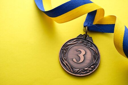 3rd place bronze medallion for a runner up in a competition or race on a blue and yellow twirled ribbon over a matching yellow background with copyspaceの写真素材