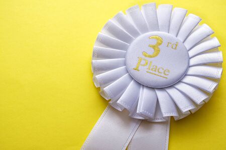 3rd place runner up white rosette with central gold text place to be awarded in a competition or race on a yellow background with copyspaceの写真素材