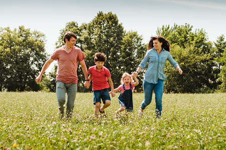 Young family with kids running hand in hand through a field or wildflowers in spring or summer approaching the camera in a healthy outdoor lifestyle concept