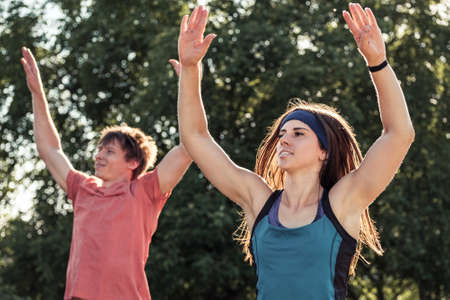 Healthy young couple exercising outdoors in a garden or park doing stretching exercises in summer sunshine in an active lifestyle conceptの写真素材