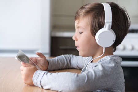 A boy with headphones and a tablet sits at a table in the kitchen.の写真素材
