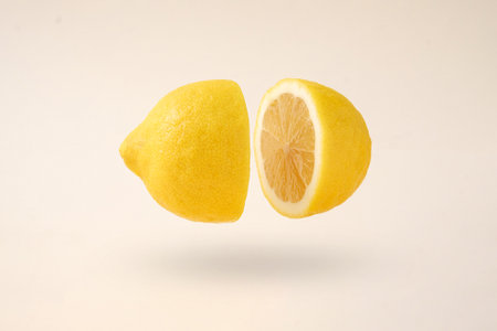 The idea of splitting into two and levitation. A cut lemon in levitation flies freely over a creamy background. Contemporary minimal concept.の写真素材