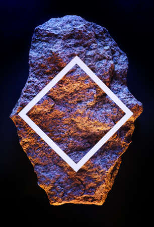 Meteorite stone in dark space with white frame of copy space neon fluorescent lighting. Contemporary...