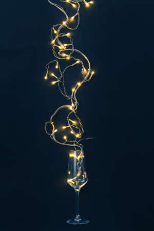 Glass of wine and garland with light bulbs on black background minimal creative party concept.の写真素材
