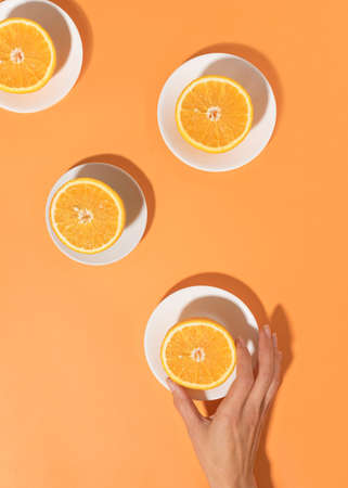 Oranges on in plates on a bright table and a woman's hand. Minimal food concept. Flat lay.