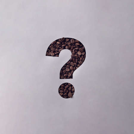 Cutout question mark in a sheet of grey paper revealing roasted coffee beans behind in a conceptual image with copy spaceの写真素材