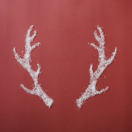 Pair of reindeer antlers formed of white winter snow over a festive red background symbolic of...