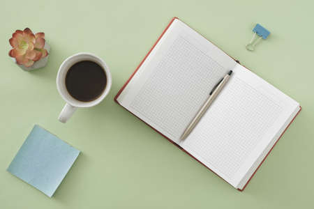 Office or business background with open notebook and ballpoint pen on green with sticky memo pad, flower and cup of coffee in a flat lay viewの写真素材