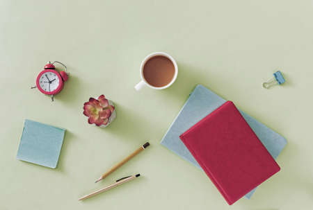 Business or office still life with open notebook or journal on a pale green background with pen, pencil, flower, mug of coffee and paper clip in an overhead viewの写真素材
