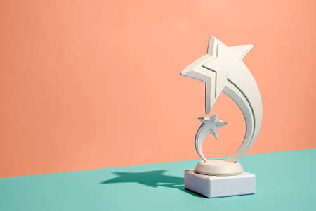 Dual shooting star trophy or ornament over a diagonal bicolor background of orange and green with copy space and shadowの写真素材