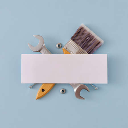 Blank white banner over crossed paint brush and spanner on a blue background in square format in a...