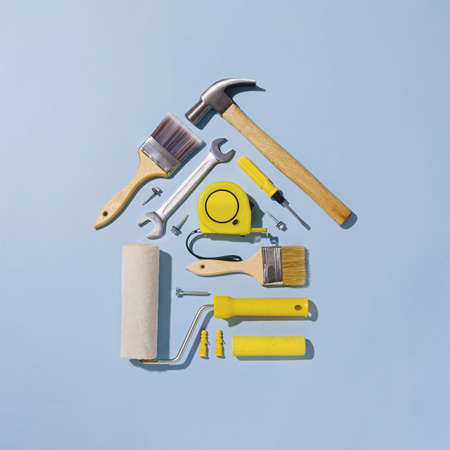Creative flat lay still life with an assortment of household tools forming a small house in a DIY, renovations, construction or maintenance concept over blueの写真素材