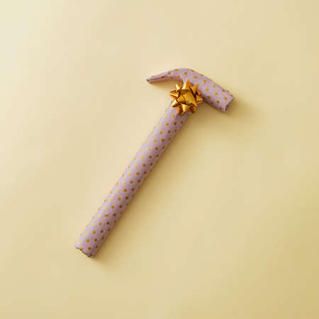Gift wrapped hammer in yellow polka dot paper decorated with a gold ribbon bow over a yellow background with copy spaceの写真素材