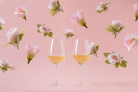 Two glasses of white wine on pink background and falling rose flowers. Concept of holiday party...