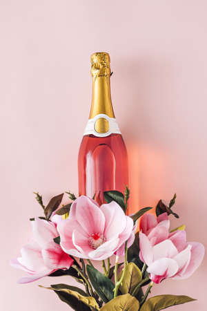 Full bottle of pink champagne with fresh flowers symbolic of love and romance over a pink background with copy spaceの写真素材