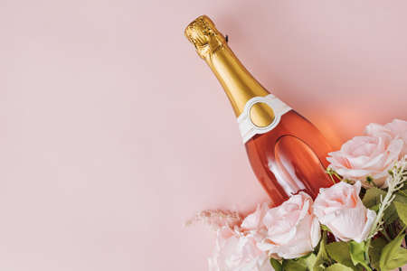 Greeting card or invitation with a bottle champagne and pink roses placed to the corner over pink with copy spaceの写真素材