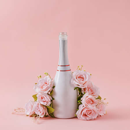 White bottle of champagne with garland of pink roses over a matching pink background with copy space for your greetingの写真素材