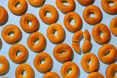 Fresh cripsy bagels background texture with one broken into four pieces arranged in diagonal lines on blueの写真素材