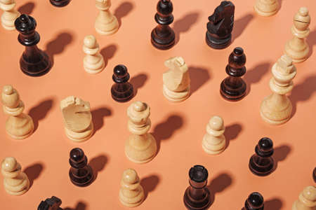 Assorted chess pieces arranged randomly on an orange background with shadow vuewed high angle