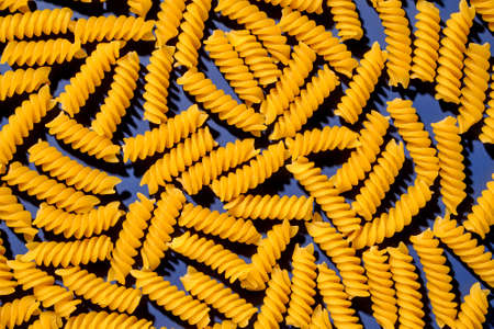 Pasta dry spiral italian yellow on blue background pattern. Flatlay and top view.