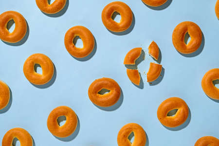Diagonal rows of fresh baked bagels with one broken into four pieces in a concept of individualityの写真素材