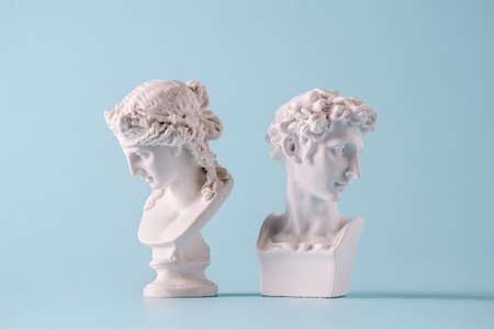 Two small antique style Roman or Grecian busts of young men facing away from each other on blueの写真素材