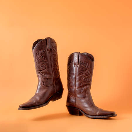Two elegant classic cowboy boots on an orange clay background. Ranger cowboy concept on a ranch in america usa texas.の写真素材