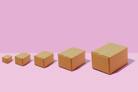 Cardboard boxes of different sizes in a row on a purple background. Parcel delivery concept.