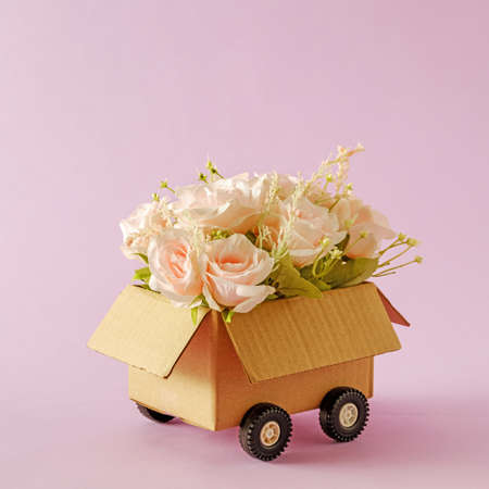 A blooming bouquet of flowers of romantic pink roses as a gift in a delivery box with truck wheels.の写真素材
