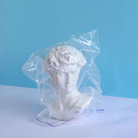 The head of an antique David statue and a plastic bag on a pastel background as a concept of isolation and plastic pollution of the environment.の写真素材