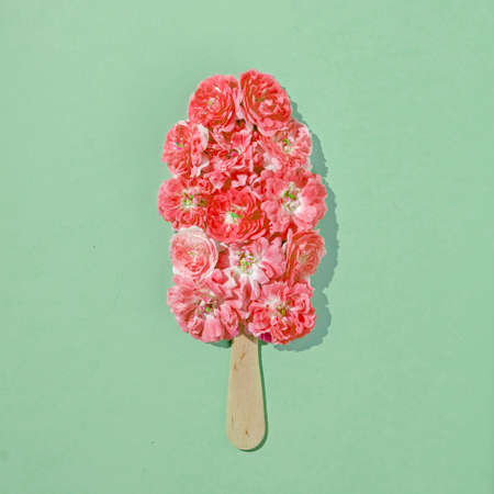 Fresh ice cream on a stick with rose flowers in summer on a pastel green background. Minimal fun food concept and metaphor.の写真素材